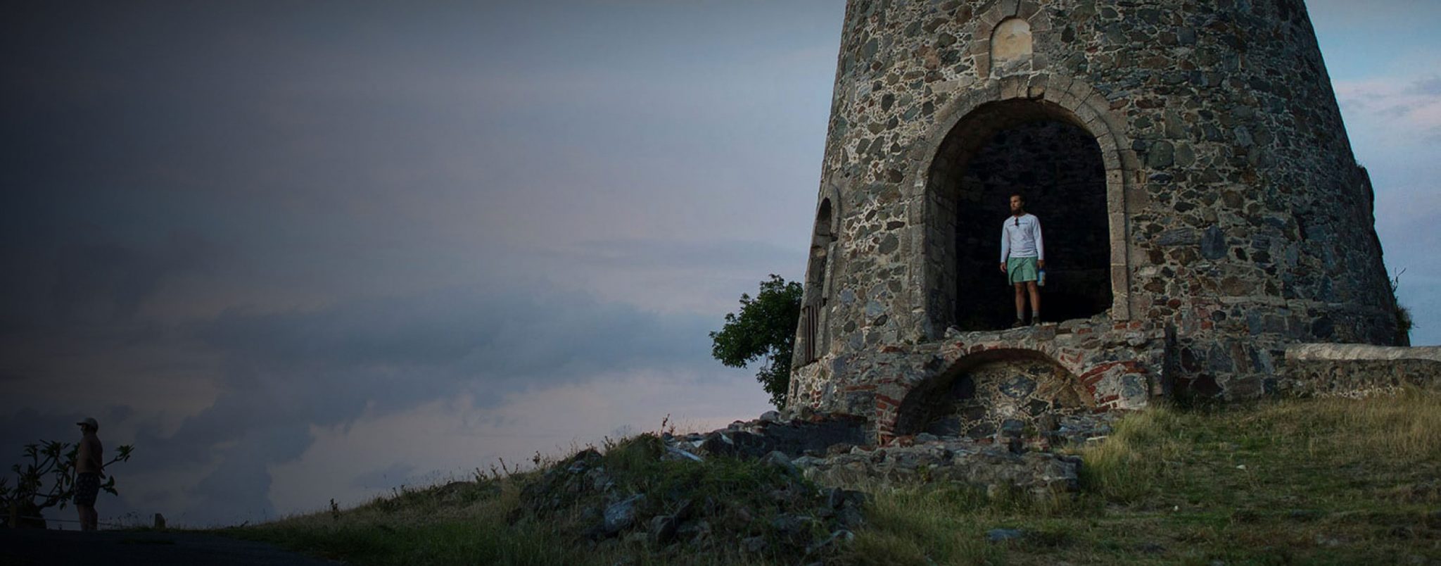 A man stands in an archway, part of a stone fortress.