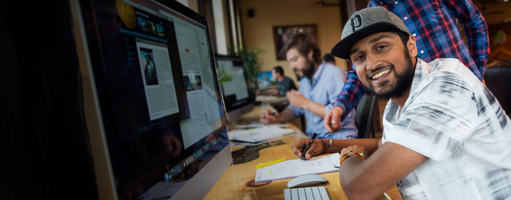 A man smiles while studying at his desk in front of a computer.